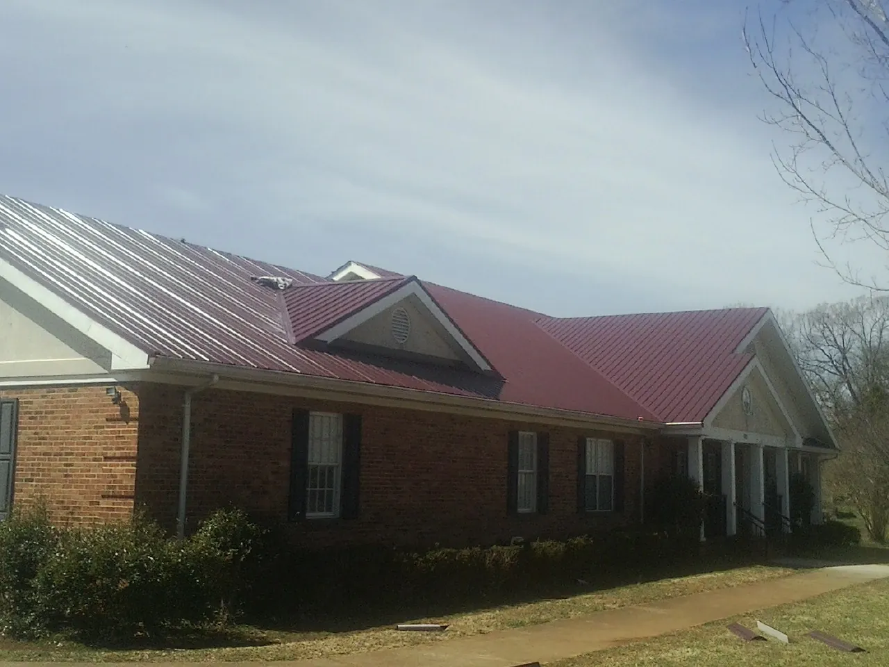 Red metal roof with gabled entries on a long brick building, from a Hail Damage Roof Repair job in Pottsboro