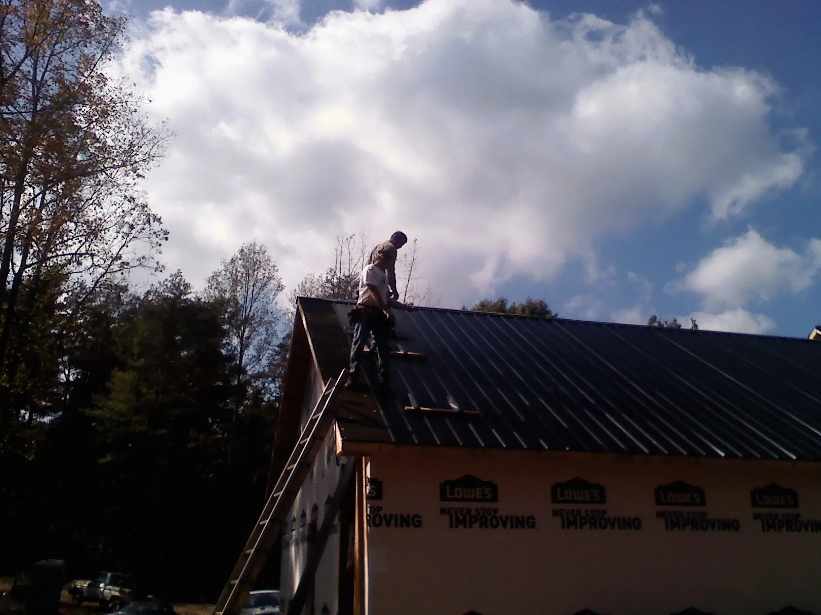 Roofer fastening dark metal panels high against a cloudy sky, from a Roof Inspection job in Pottsboro