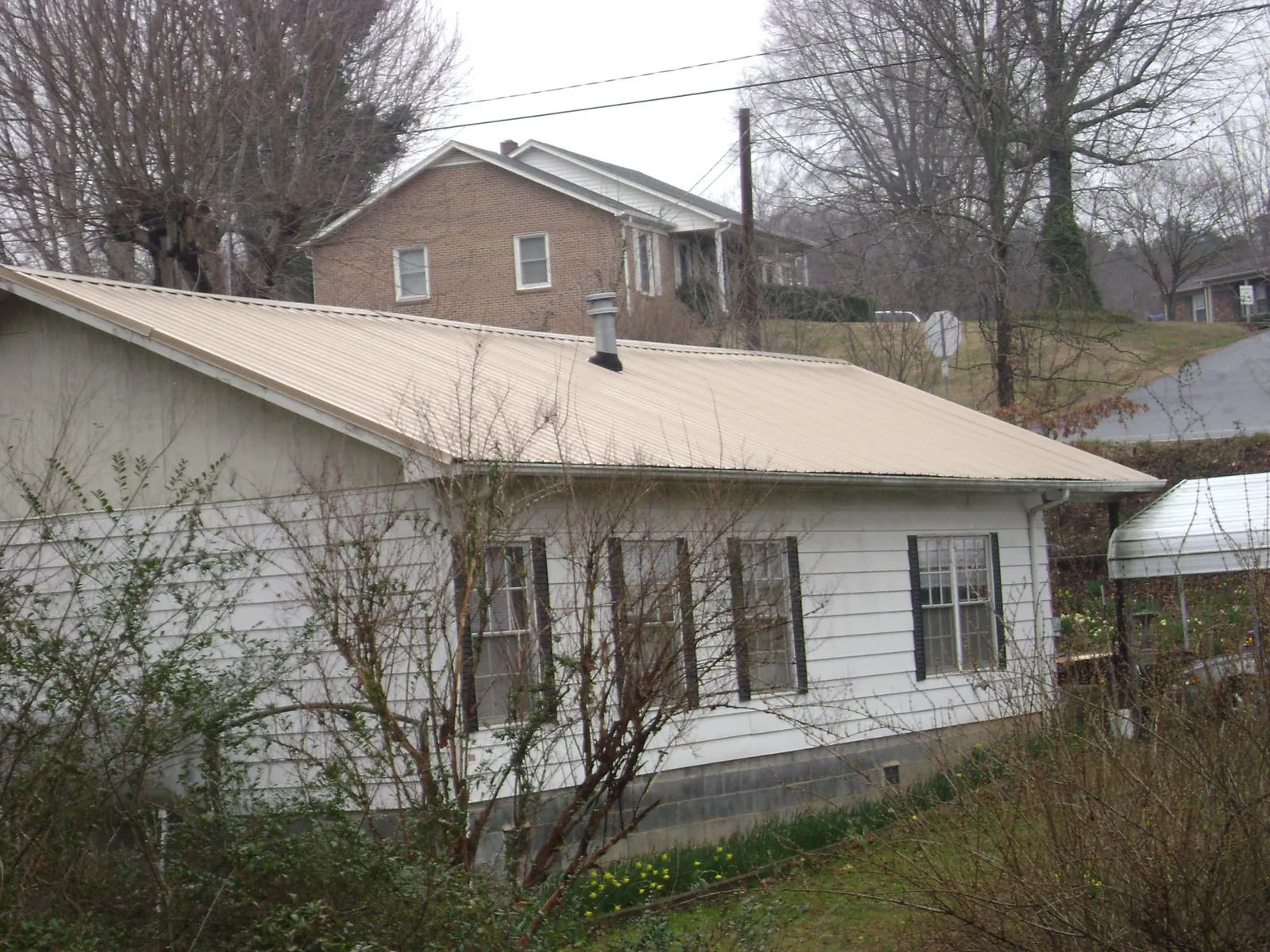 Tan metal roof on a white sided house set into a hillside — Commercial Roofing by Roofing Brothers in Pottsboro